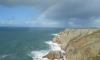 A rainbow is created from the storm waves crashing against a high cliff